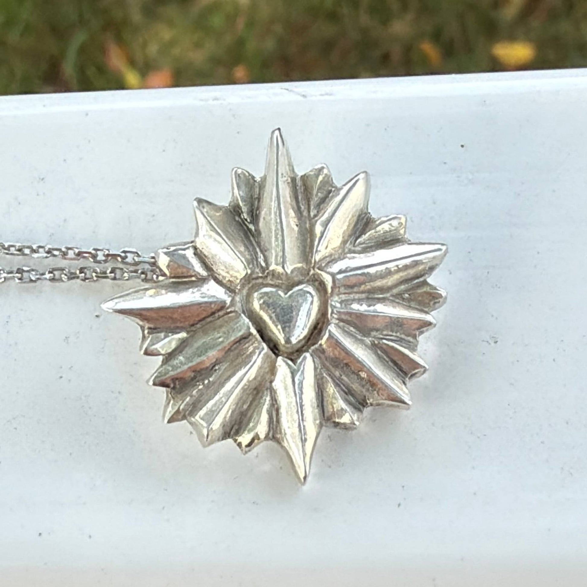 Sterling silver star-shaped pendant with a heart in the center on a white surface.