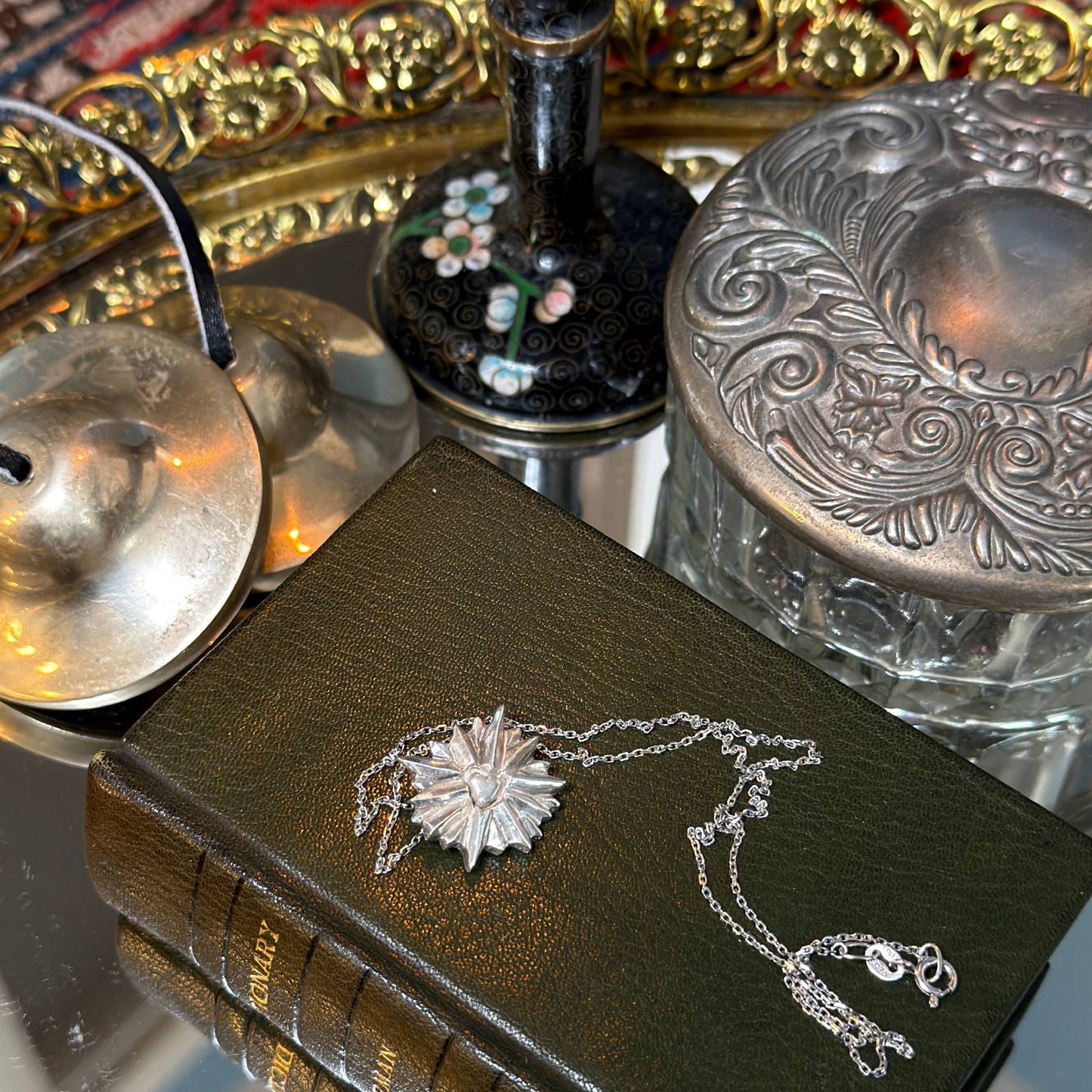 Decorative book with a silver necklace on top, surrounded by ornate objects.